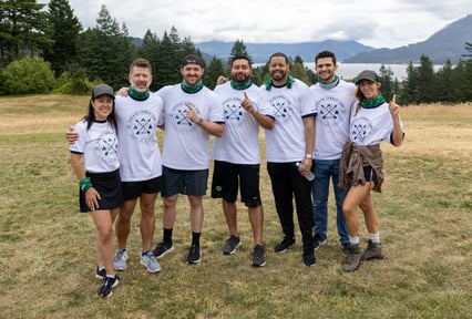 Attendees at a franchising event pose together outdoors in branded t-shirts with scenic mountain views behind them.