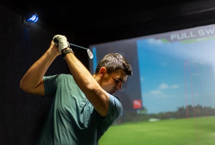 Man practicing a golf swing inside an indoor golf simulator.