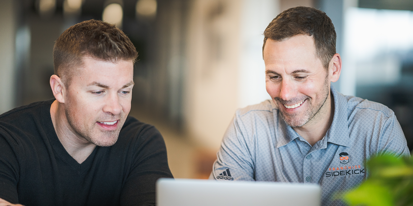 Two men smiling looking at a laptop screen
